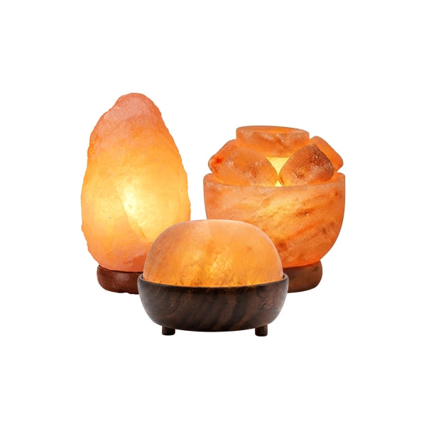 Three glowing salt lamp products arranged together on a white background: a tall natural salt crystal lamp, a cluster of salt stones with a candle-like light inside, and a dome-shaped salt lamp in a dark wooden base.